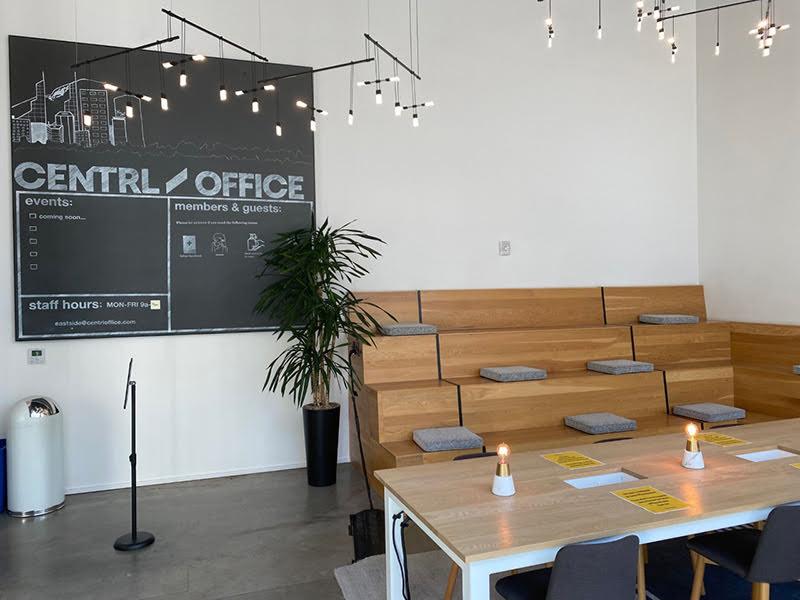 A room with stair benches, concrete floor, and a large table in the foreground; a blackboard on a white wall reads Centrl / office events.